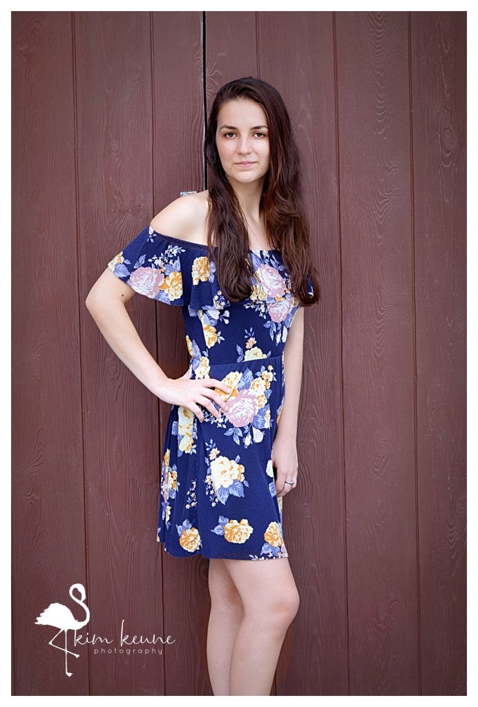 teenage girl posing in front of red barn door wearing a floral dress